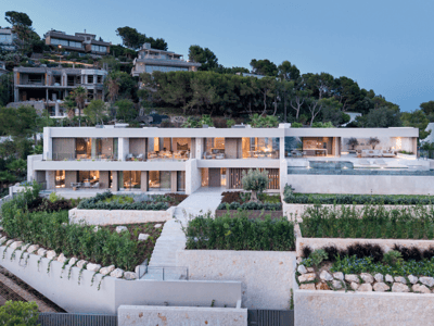 Villa moderna de dos plantas con piscina infinita, jardines de piedra y fachada de cristal iluminada al anochecer.