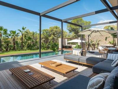 Modern terrass med grå soffor, träbord och pool framför en frodig tropisk trädgård.