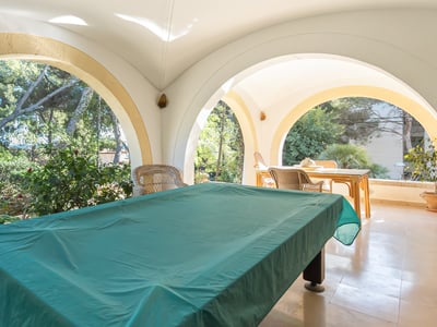 Gran terraza cubierta con arcos blancos, una mesa de billar con mantel verde y vistas al jardín.