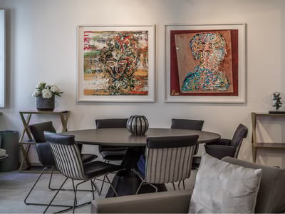 Comedor moderno con mesa redonda oscura, sillas de diseño y dos grandes cuadros abstractos en la pared blanca.