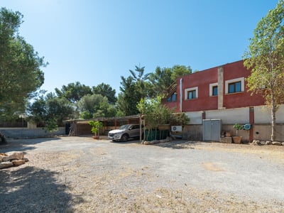Una amplia zona de aparcamiento de grava frente a un edificio rojo con un coche plateado bajo un porche de madera.