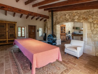 Gran mesa con mantel rosa en una estancia rústica con vigas de madera, paredes de piedra y estufa de leña.
