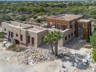 Vista elevada de una gran villa de lujo con paredes de piedra en construcción rodeada de vegetación mediterránea.