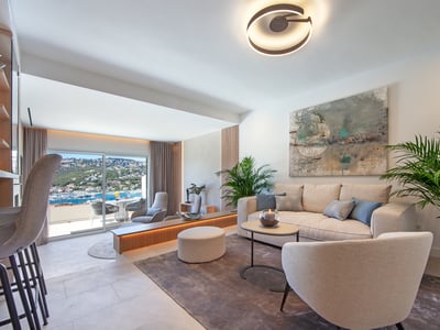 Salón moderno y luminoso con muebles crema, grandes ventanales al mar y plantas de interior.