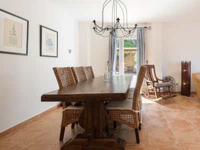Amplio salón-comedor con mesa de madera maciza, sillas de mimbre, suelo de terracota y acceso a la terraza.