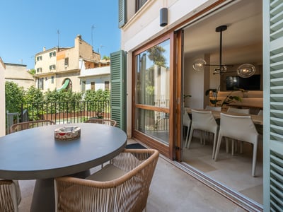 Sonnige Terrasse mit grauem Esstisch und Korbstühlen neben großen Glasschiebetüren.