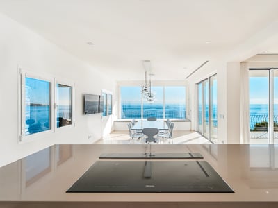 Närbild på köksö med induktionshäll med utsikt över matplats och stora fönster mot det blå havet.