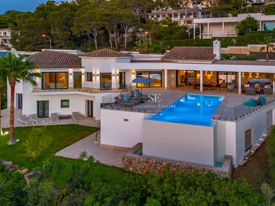 Amplio salón con ventanales, sofás beige, chimenea moderna y vistas panorámicas. Iluminación natural abundante.