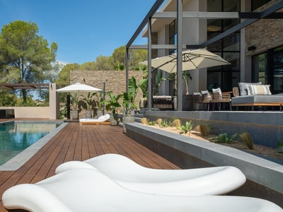 Lyxig utomhuspool med trädäck, vita designsolsängar och stenmurar under en klarblå himmel.