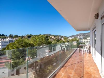 Larga terraza con barandillas de cristal y suelo de terracota con vistas a colinas verdes bajo un cielo azul despejado.