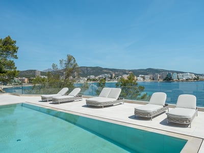 Modern white terrace with a turquoise pool, loungers, and a glass railing overlooking a scenic Mediterranean bay.