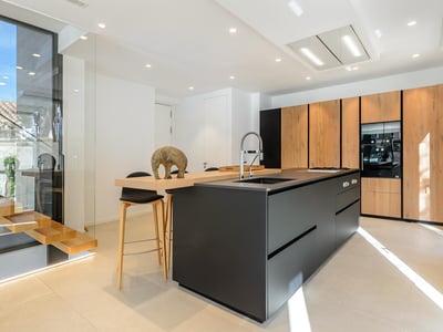 Cocina moderna con una gran isla negra, armarios de madera y electrodomésticos integrados bajo iluminación brillante.