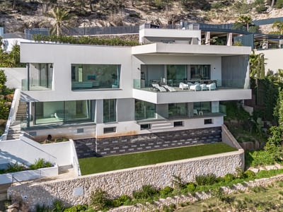 Villa blanche moderne de plusieurs étages avec de grandes baies vitrées et terrasses construite sur une colline rocheuse.