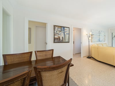 Salón abierto con sofá de cuero crema, mesa de comedor de madera y grandes ventanales con vistas a la montaña.