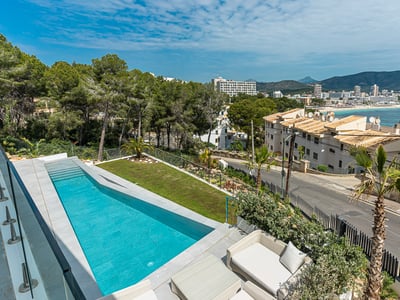 A long turquoise swimming pool on a terrace with glass railings, overlooking a coastal town and distant mountains.