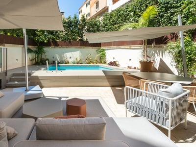 Moderne Terrasse mit türkisem Pool, Holzdeck, grauen Sofas und Sonnenschirmen unter klarem Himmel.