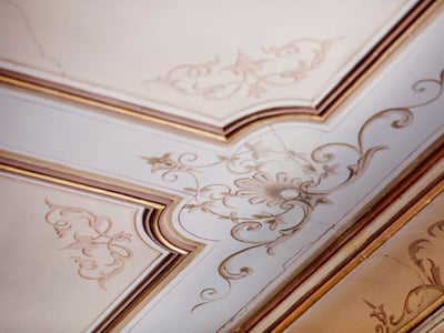 Verzierte Deckenleisten mit handbemalter floraler Filigranarbeit in Creme und Gold.