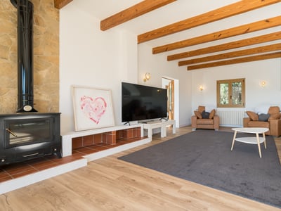 Acogedor salón con vigas de madera a la vista, estufa de leña negra, sofás de cuero y una televisión grande.