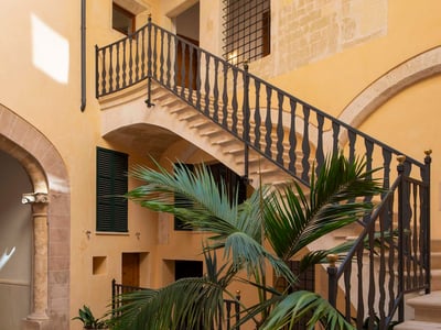 Traditioneller Innenhof mit gelben Wänden, Steintreppe mit Eisengeländer und einer zentralen Palme.