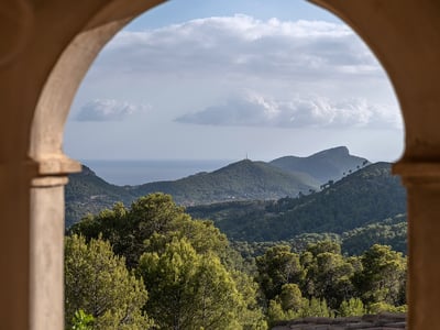 A view of lush green mountains and the distant sea framed by a traditional stone archway.