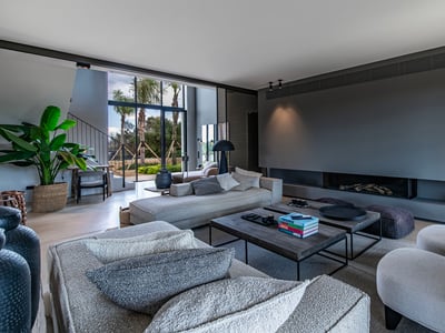 Amplio salón de diseño minimalista con sofás grises, chimenea empotrada y vistas a palmeras a través de grandes ventanales.