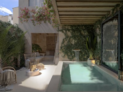 Private plunge pool with waterfall feature surrounded by ivy walls, bougainvillea, and wicker seating under a pergola.