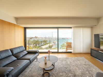 Modern living room featuring a black leather sofa and large glass sliding doors overlooking a harbor with many boats.