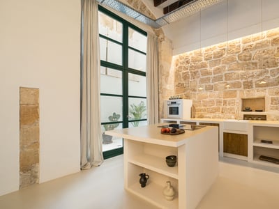 Cuisine moderne avec îlot blanc, mur en pierre rustique, hauts plafonds et grandes fenêtres.