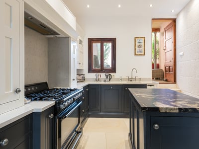 Cocina con gabinetes azul marino, encimeras de mármol blanco, estufa Smeg y una pared de piedra natural.