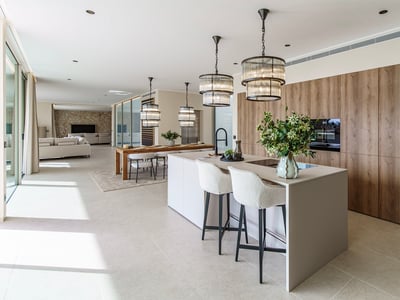 Cocina moderna con una isla grande, taburetes blancos, lámparas de diseño y muebles de madera en un espacio abierto.