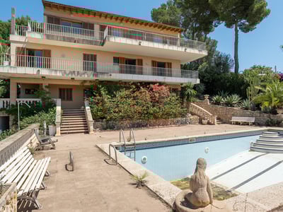 Multi-level Mediterranean villa featuring large terraces and a large empty swimming pool surrounded by lush greenery.