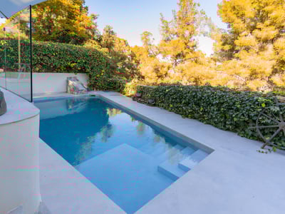 Piscina turquesa con escalones integrados, rodeada de suelos de piedra clara y paredes de hiedra verde.