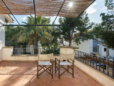 Terraza soleada con suelo de terracota, sillas de director, barandilla de hierro y techo de cañizo bajo el sol.