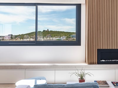 Salón moderno con pared de madera, chimenea integrada y ventanal con vistas a una colina con un castillo.