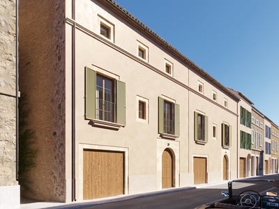 Beige stucco building with green shutters, wooden garage doors, and a classic car on a sunlit street.