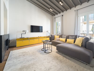 Modern living room featuring a grey sectional sofa with yellow cushions, vaulted beamed ceiling, and a fireplace.
