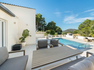 Rymlig solindränkt terrass med en rektangulär pool, eleganta loungemöbler och lummig grönska.