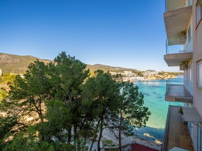 Balcones de apartamentos con vistas a una bahía mediterránea turquesa con pinos y cielo azul despejado.