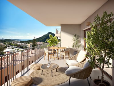Balcón moderno con muebles de mimbre, mesa de comedor y plantas con vistas a un pueblo costero y colinas verdes.