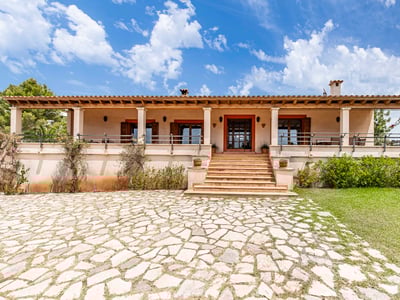 Vista frontal de una villa mediterránea de una planta con entrada de piedra, escaleras y terraza cubierta.