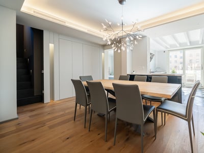 Modern dining room with a large light wood table, eight charcoal chairs, and a branch-style chandelier.
