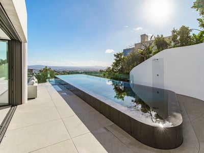 Une piscine à débordement élégante sur une terrasse blanche minimaliste surplombant la ville sous un ciel bleu.