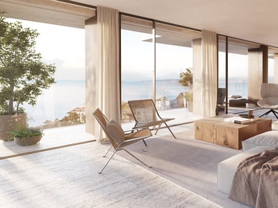 Ljust minimalistiskt vardagsrum med fönster från golv till tak med utsikt över havet, stor soffa och träbord.