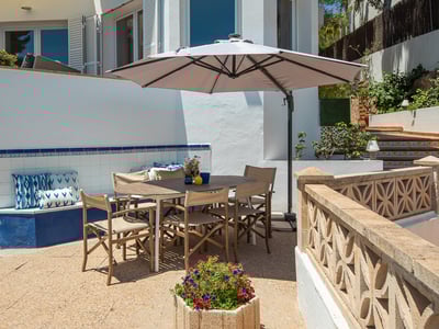 Sunny terrace featuring a wooden table, umbrella, blue tiled bench, and decorative stone balustrade.