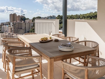 Moderne Terrasse mit Holztisch, geflochtenen Stühlen und Panoramablick auf Meer und Stadt.