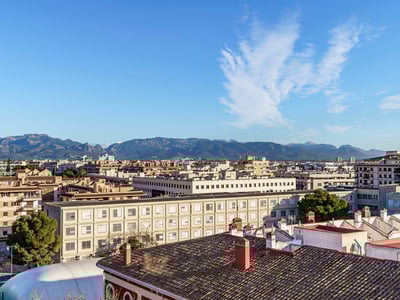 Vista elevada sobre los tejados de la ciudad hacia una cordillera bajo un cielo azul despejado.