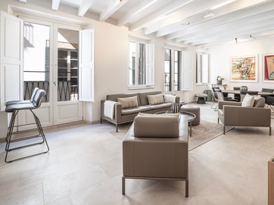 Salón espacioso con sofás de cuero topo, techos de vigas blancas y grandes ventanales con contraventanas.