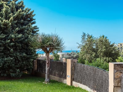 Poolansicht mit Liegestühlen, Palmen und moderner Villa im Hintergrund. Klarer blauer Himmel und üppige Vegetation.