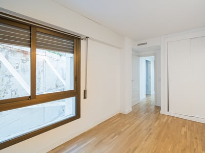 Habitación vacía con suelos de madera clara, un armario empotrado blanco y una ventana grande con marco de bronce.