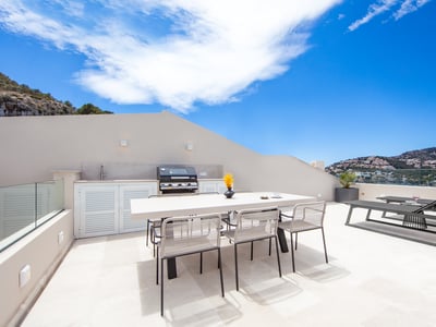 Terraza moderna con cocina exterior, mesa de comedor y tumbonas con vistas panorámicas a la costa.